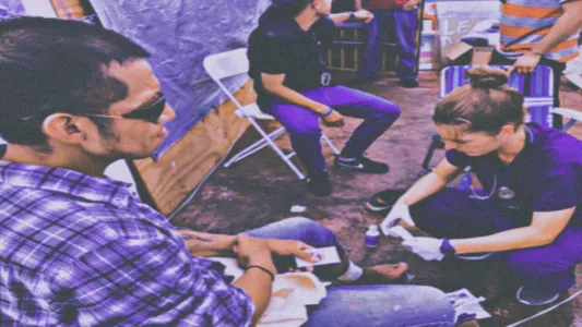 Devi Machete - A medical professional from Refugee Health Alliance treats a patient’s leg wound at the free medical clinic held at Contra Viento Y Marea. November 17, 2019. Tijuana, Mexico.