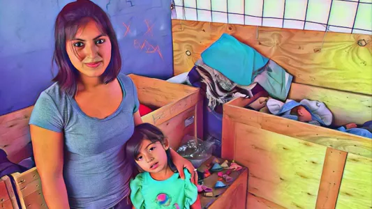 Devi Machete - A young woman and her small daughter pose for the camera while her baby boy sleeps in the clothing donation bin in the background of the rooftop donations bodega. They are receiving free donations of toys, diapers and clothing from Contra Viento Y Marea. July 6, 2019. Tijuana, Mexico.